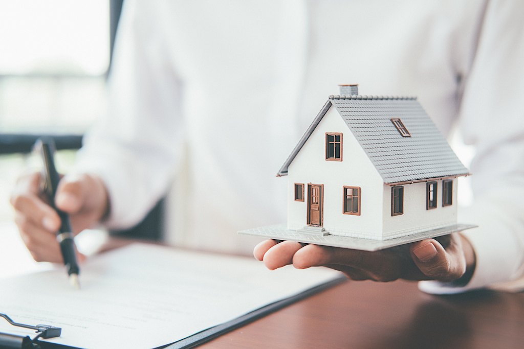 Man Writing a Home Loan With a Model House in His Hand